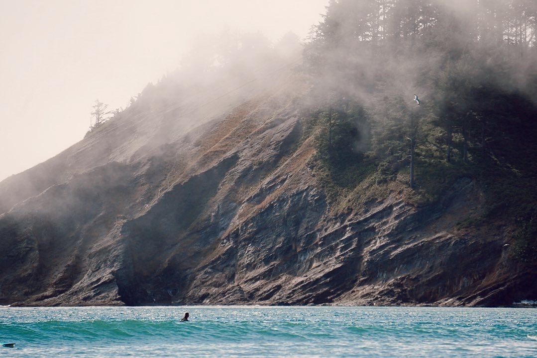 Fog moving over a coastal cliff, a lone swimmer in the water below