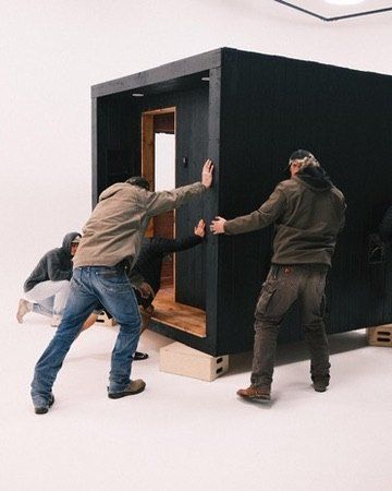 The crew pushing a finished sauna across the shop floor