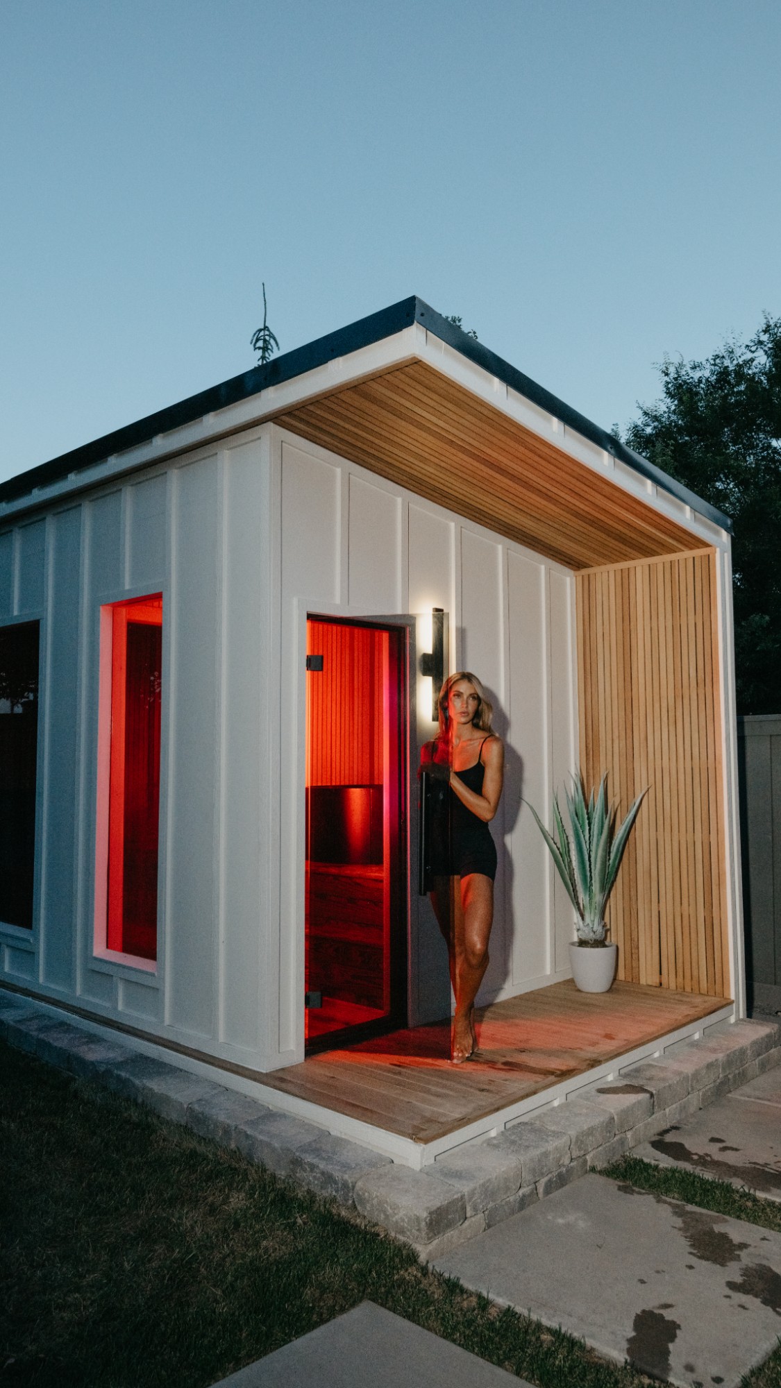 Cara Loren stepping out of the sauna at dusk, red light coming through the open door