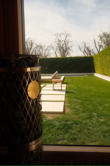 Garden view through the full-height sauna glass beside the IKI heater
