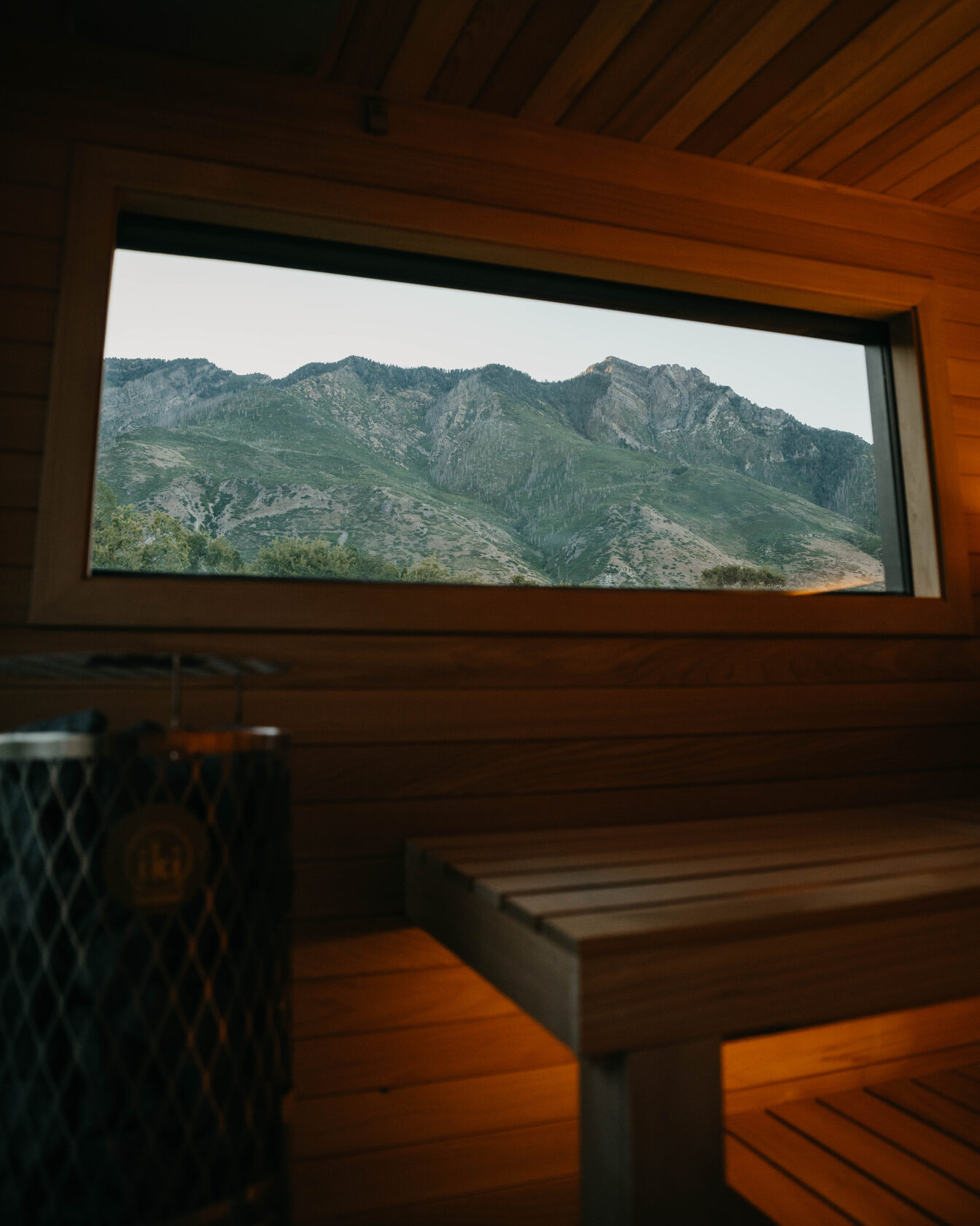 212 sauna interior, cedar bench and stone heater beneath a mountain-view window