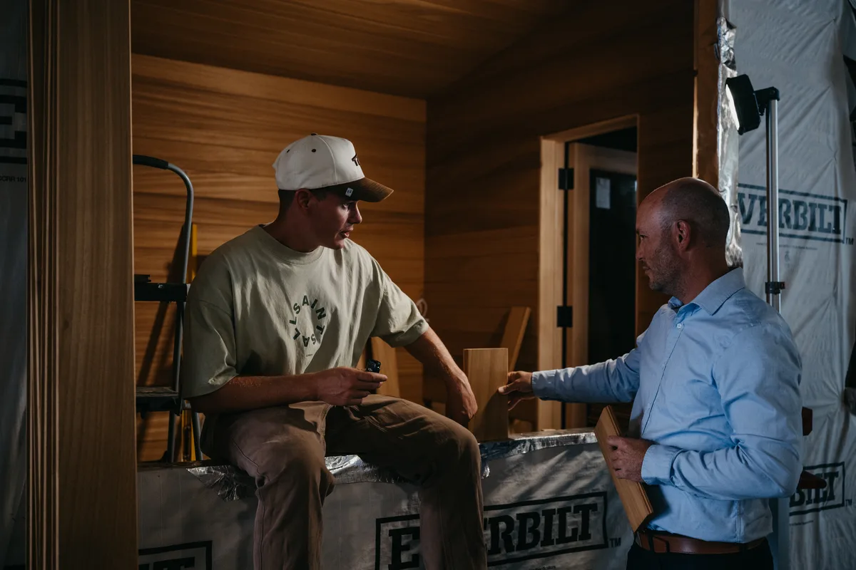 Two of the New Primitive team checking a cedar board against a sauna interior, mid-build