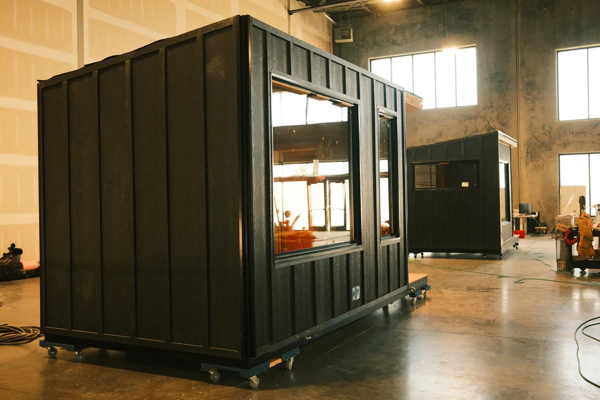 Two charred-cedar saunas on casters on the New Primitive factory floor, mid-build