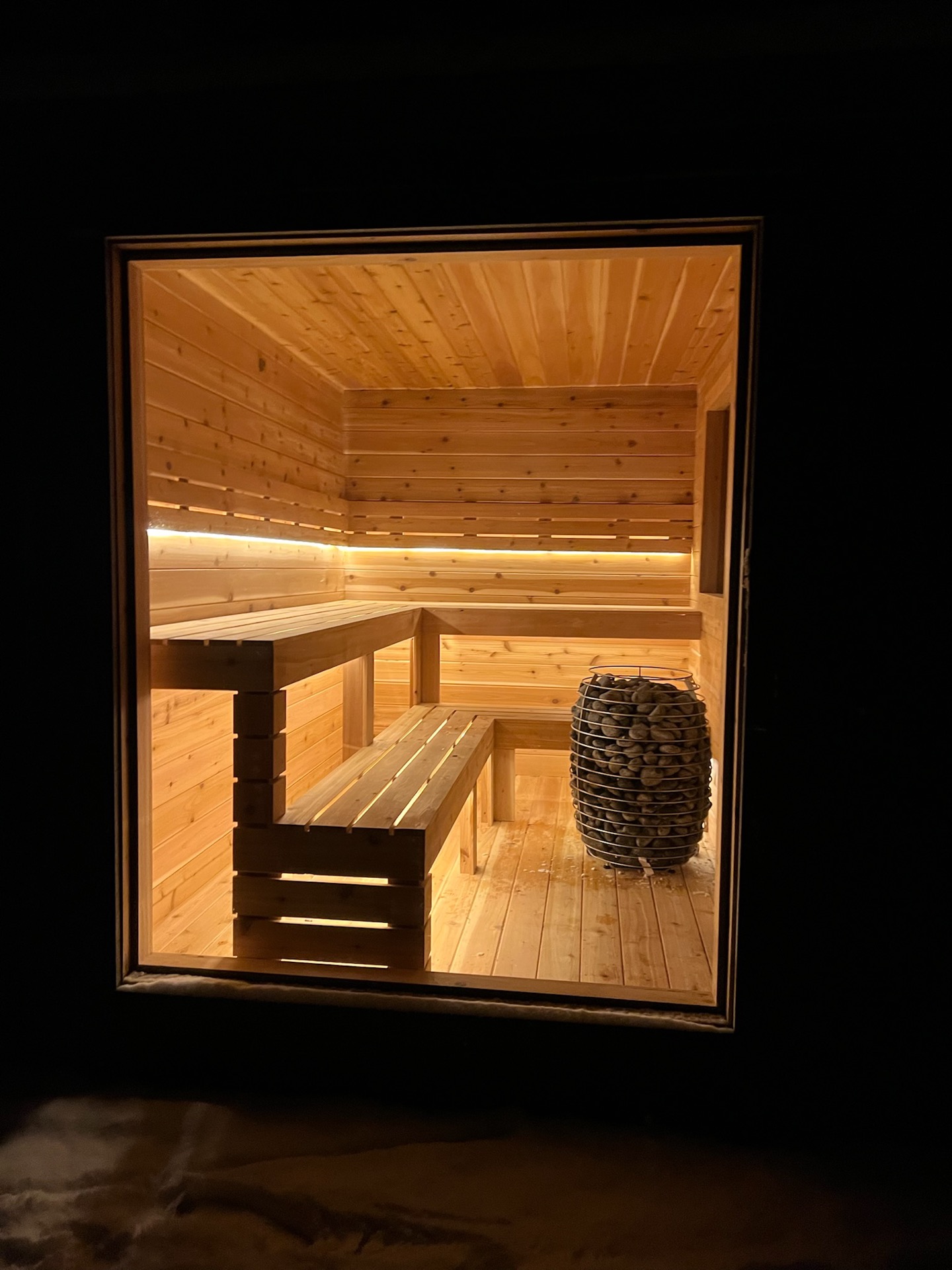 A cedar sauna interior framed through a window at dusk