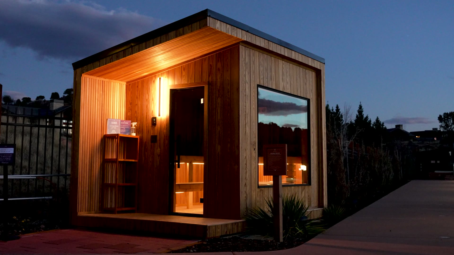 A New Primitive outdoor sauna with a warmly lit cedar entrance at dusk